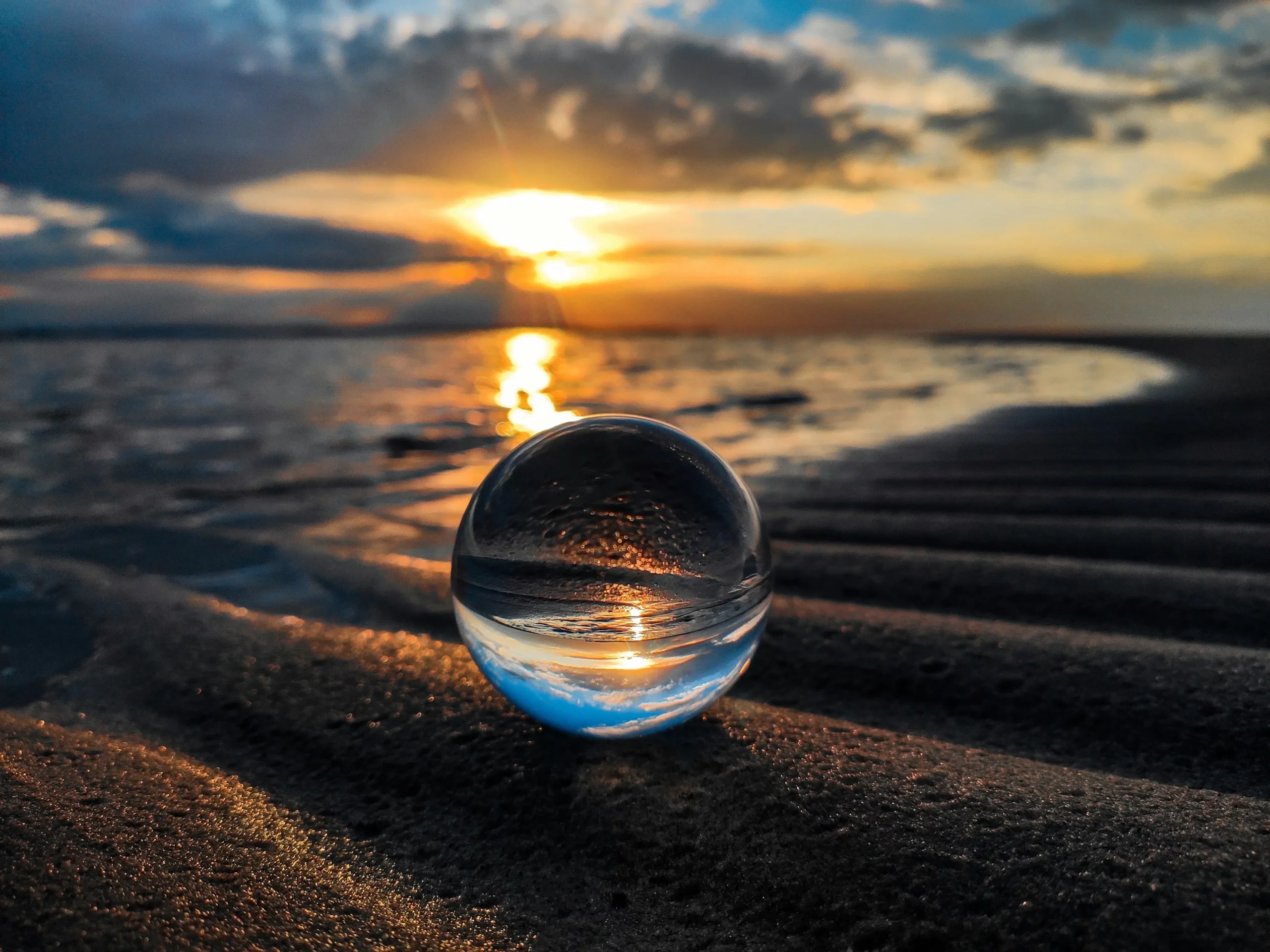 A glass ball reflecting the vibrant colors of a sunset on a serene beach.